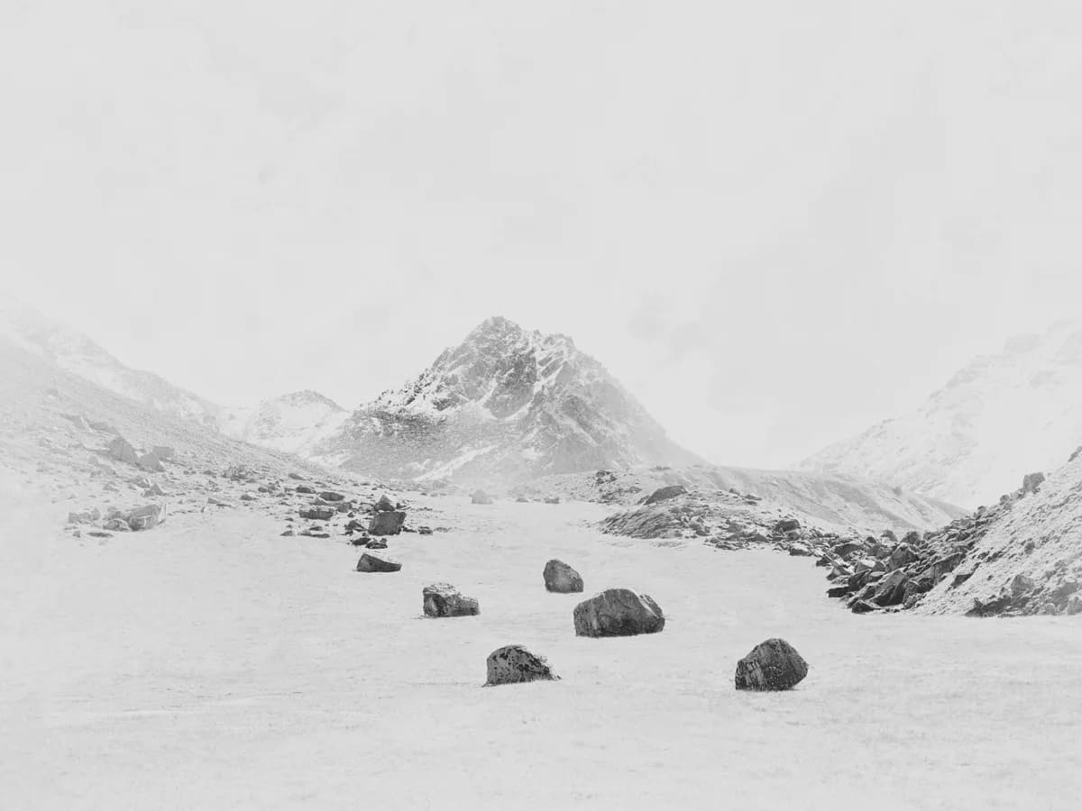 Snowy landscape with a mountain and scattered rocks. From Peak by Bastiaan Woudt.